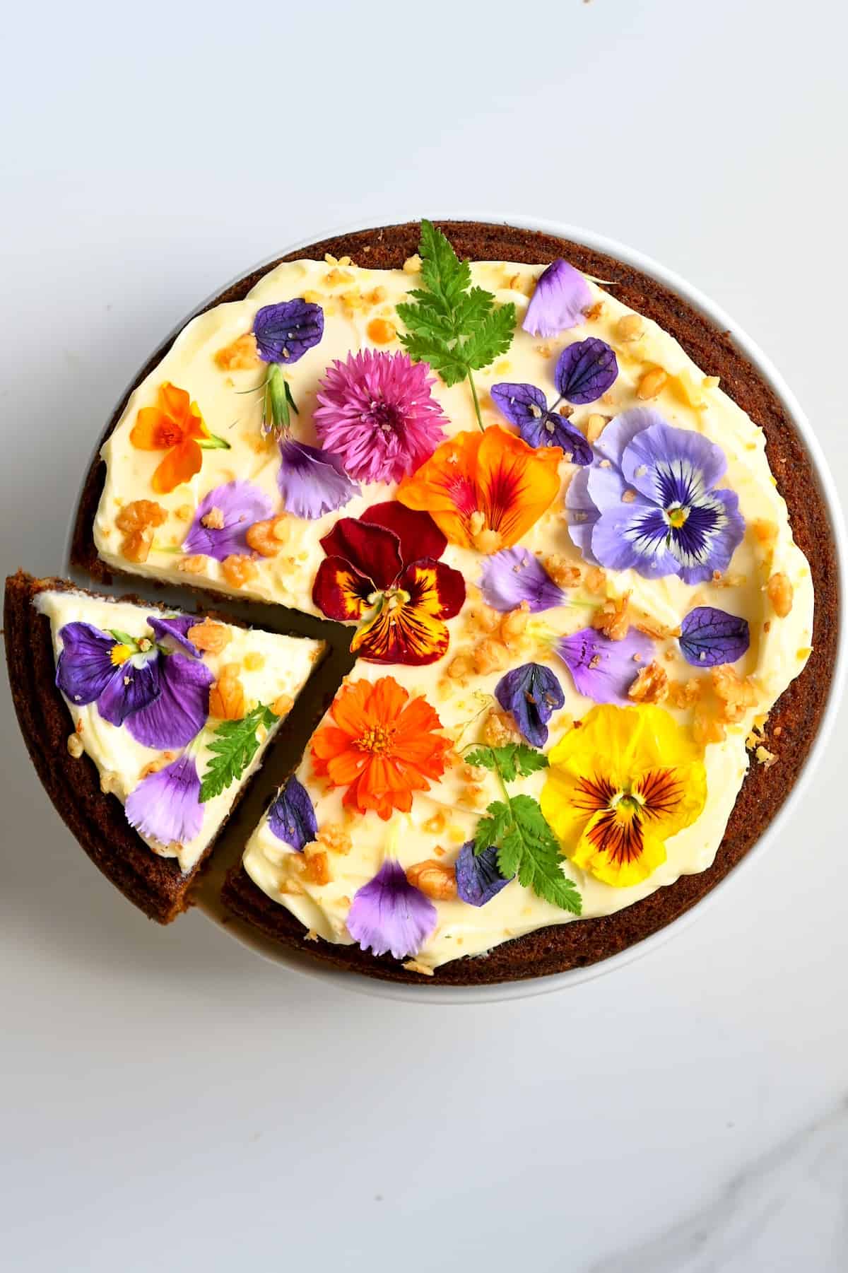 Carrot Cake with frosting and edible flowers and a cut slice