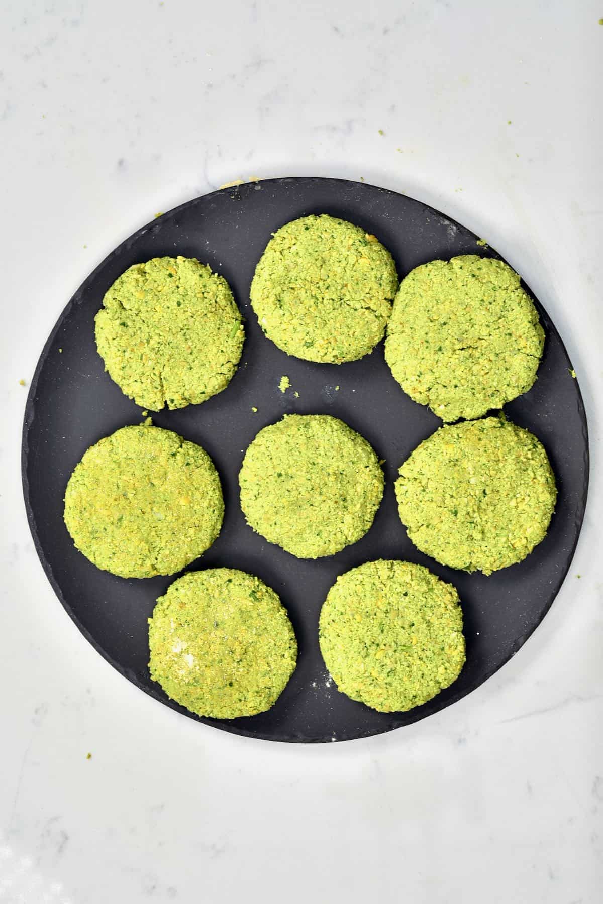 Eight uncooked falafel patties on a black plate
