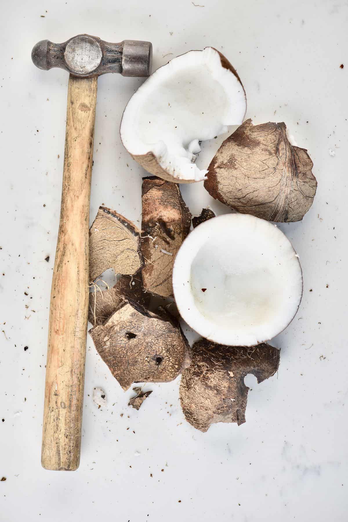 A coconut with broken shell and a hammer next to it
