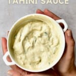 Two hands holding a bowl with tahini sauce