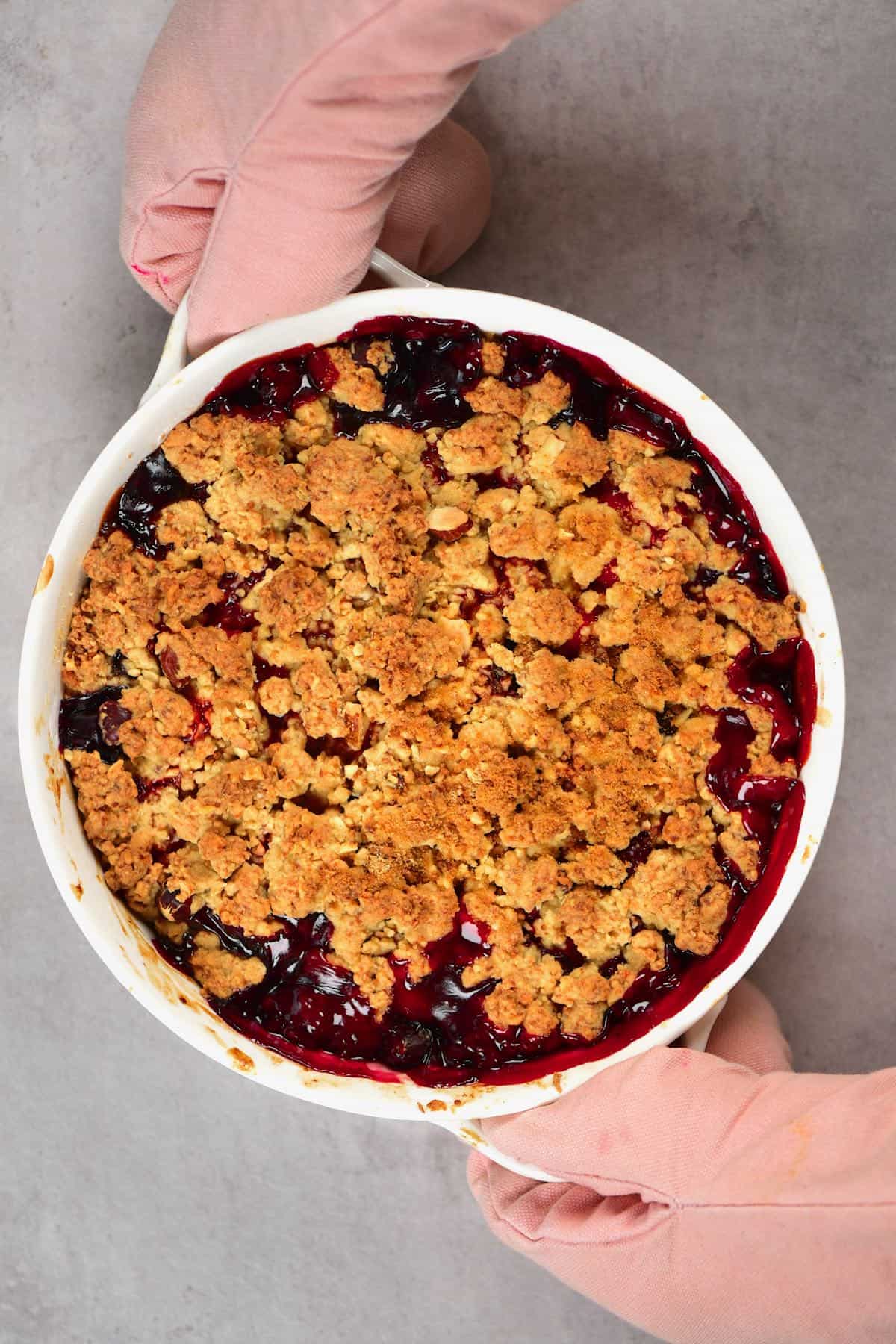Gloved hands holding a baking dish with berry crumble