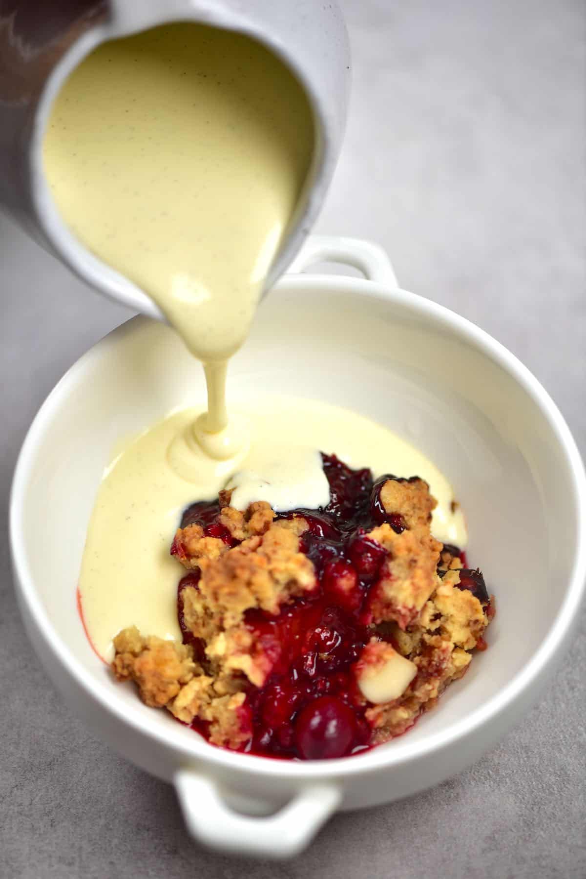 Pouring custard over berry crumble