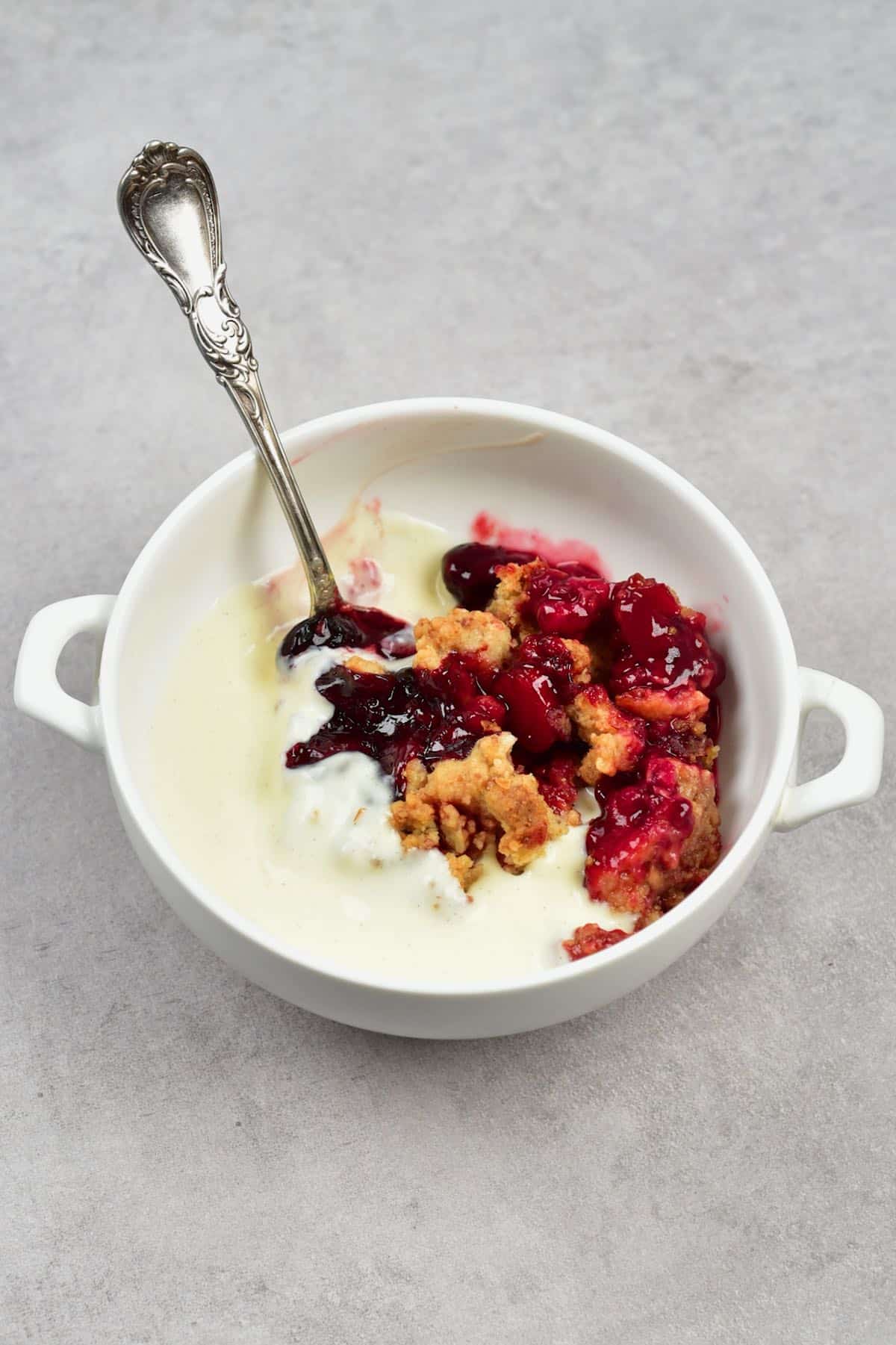 A small bowl with berry crumble and custard