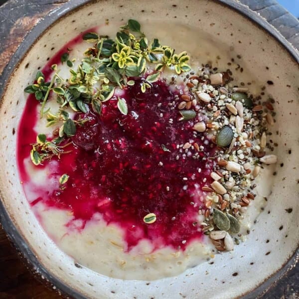 A bowl with berry oatmeal topped with seeds and herbs