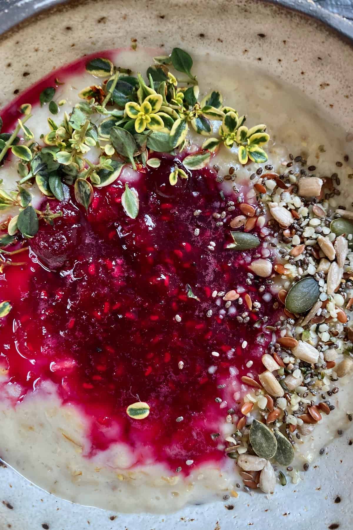 A bowl with berry oatmeal topped with seeds and herbs