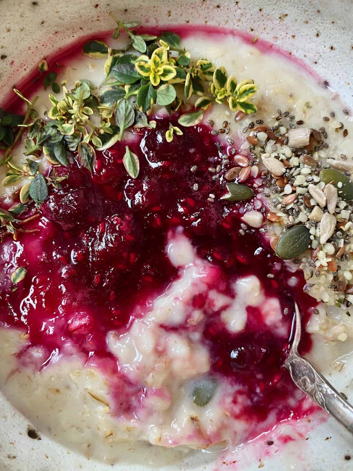A bowl with berry oatmeal topped with seeds and herbs and a spoon