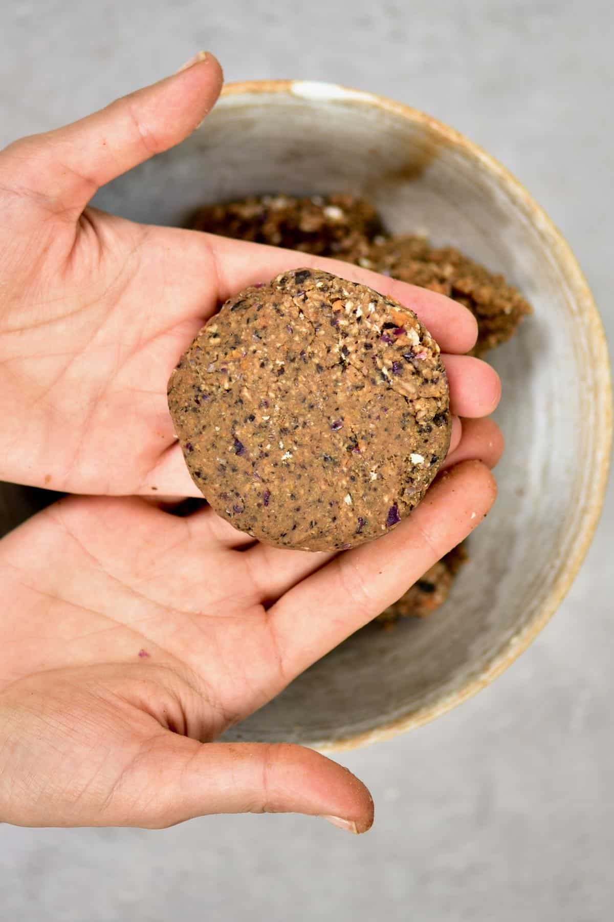Two hands holding an uncooked black bean burger patty