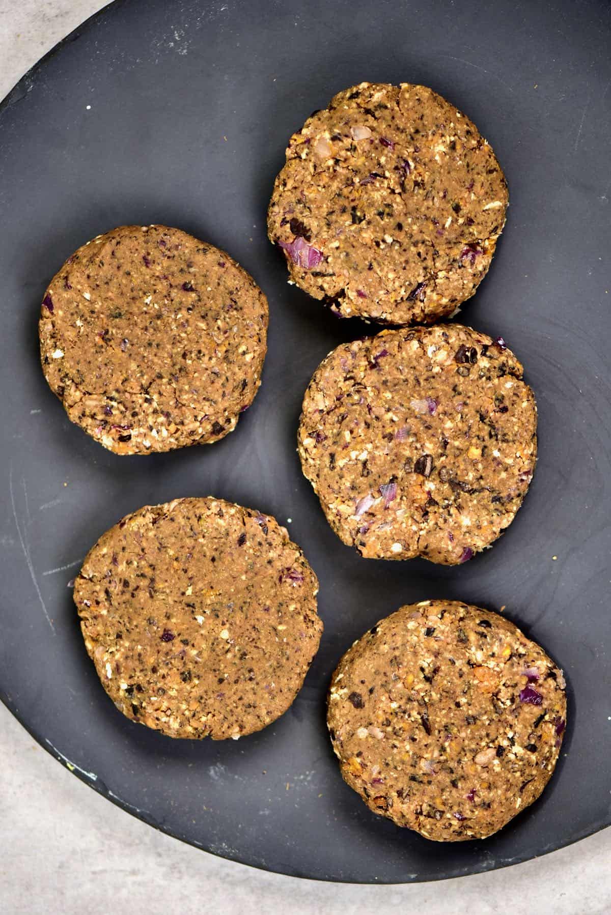 Five black bean burger patties in a black plate