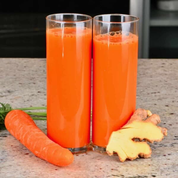 Two glasses with carrot ginger juice and a carrot and ginger next to them