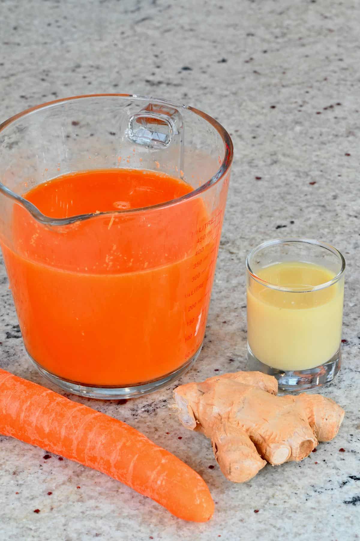 Carrot juice in a measuring cup and ginger juice in a small glass