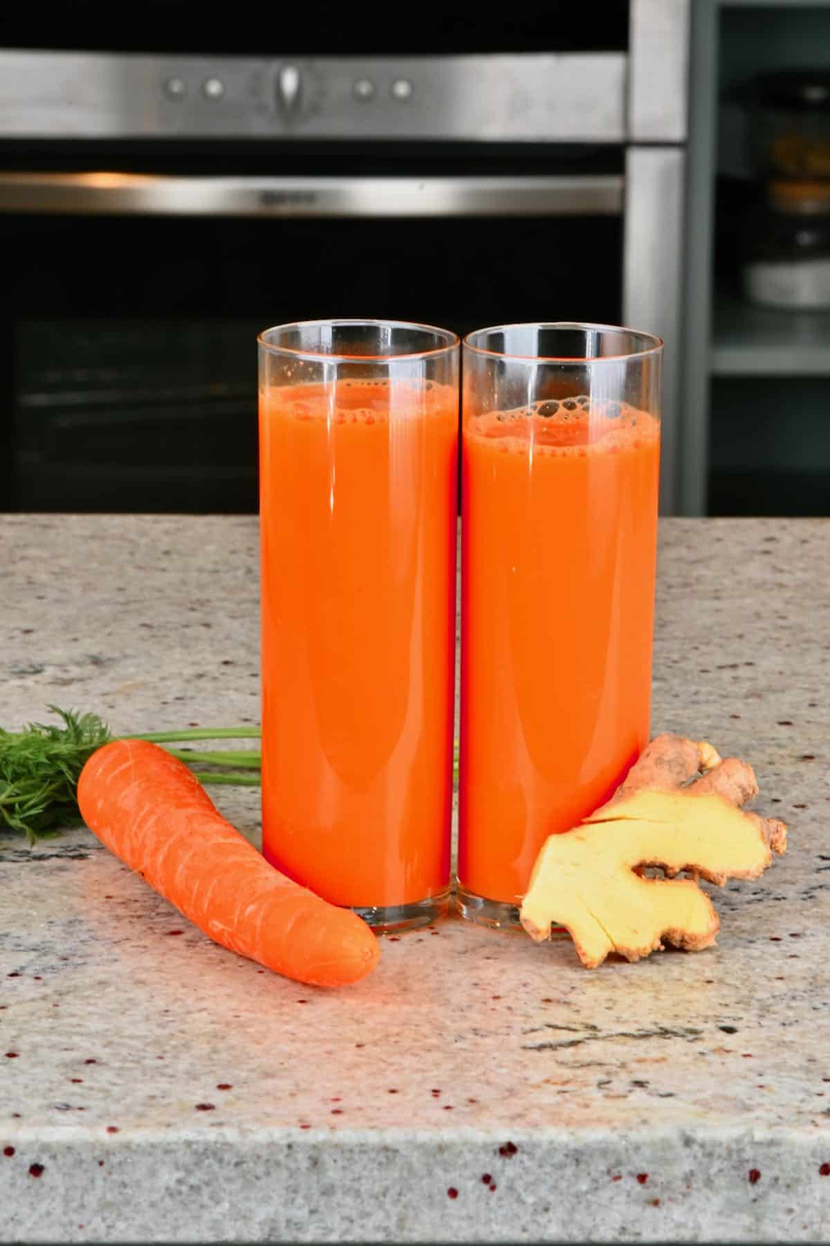 Two glasses with carrot ginger juice and a carrot and ginger next to them
