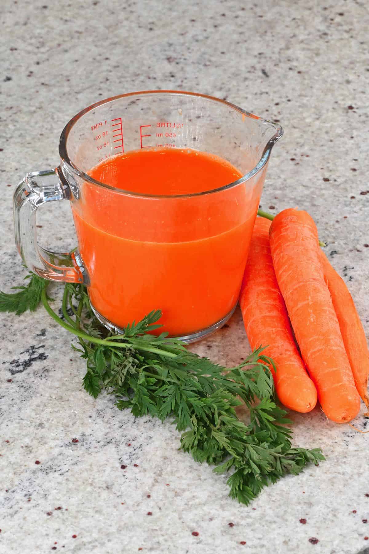 Carrot juice in a measuring cup with some carrots next to it