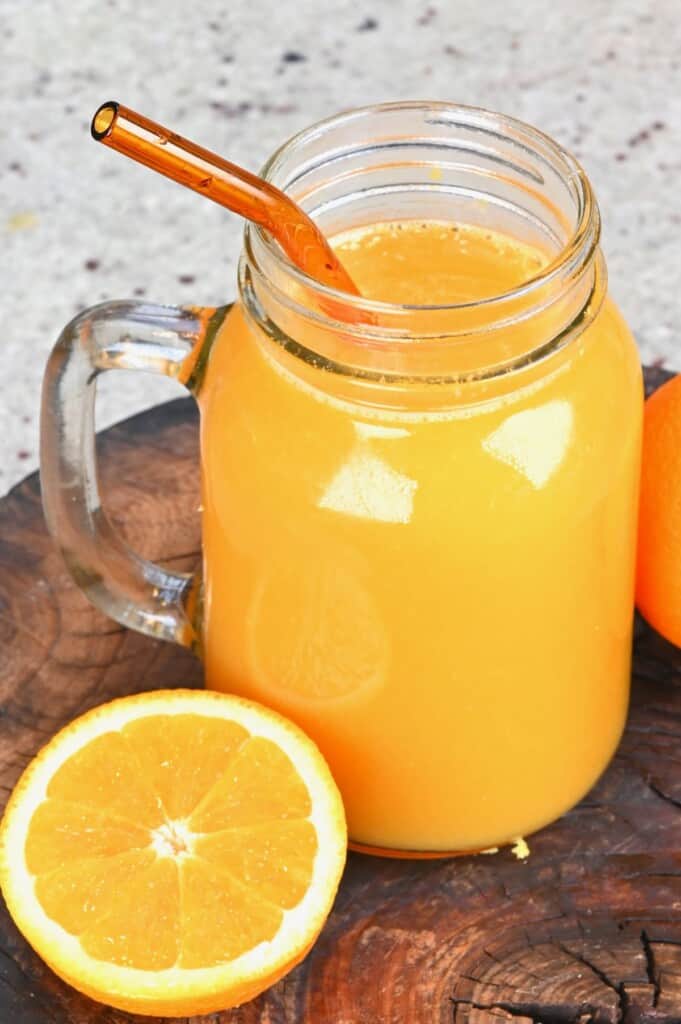 A mason jar with orange juice and a glass straw