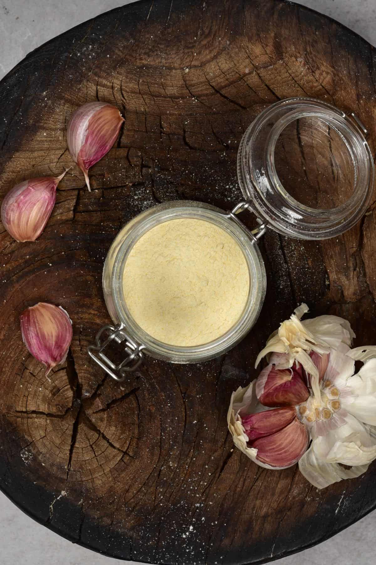 Garlic powder in a jar and some garlic cloves on a wooden board