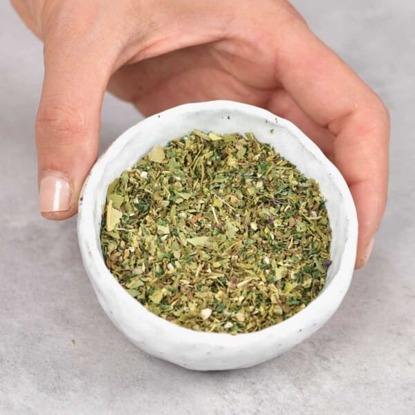 A hand holding a small bowl with Italian seasoning