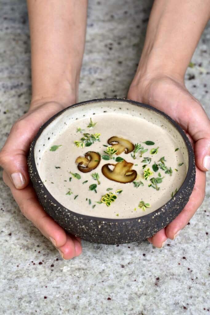 Hands holding a bowl with mushroom soup topped with three slices of mushrooms