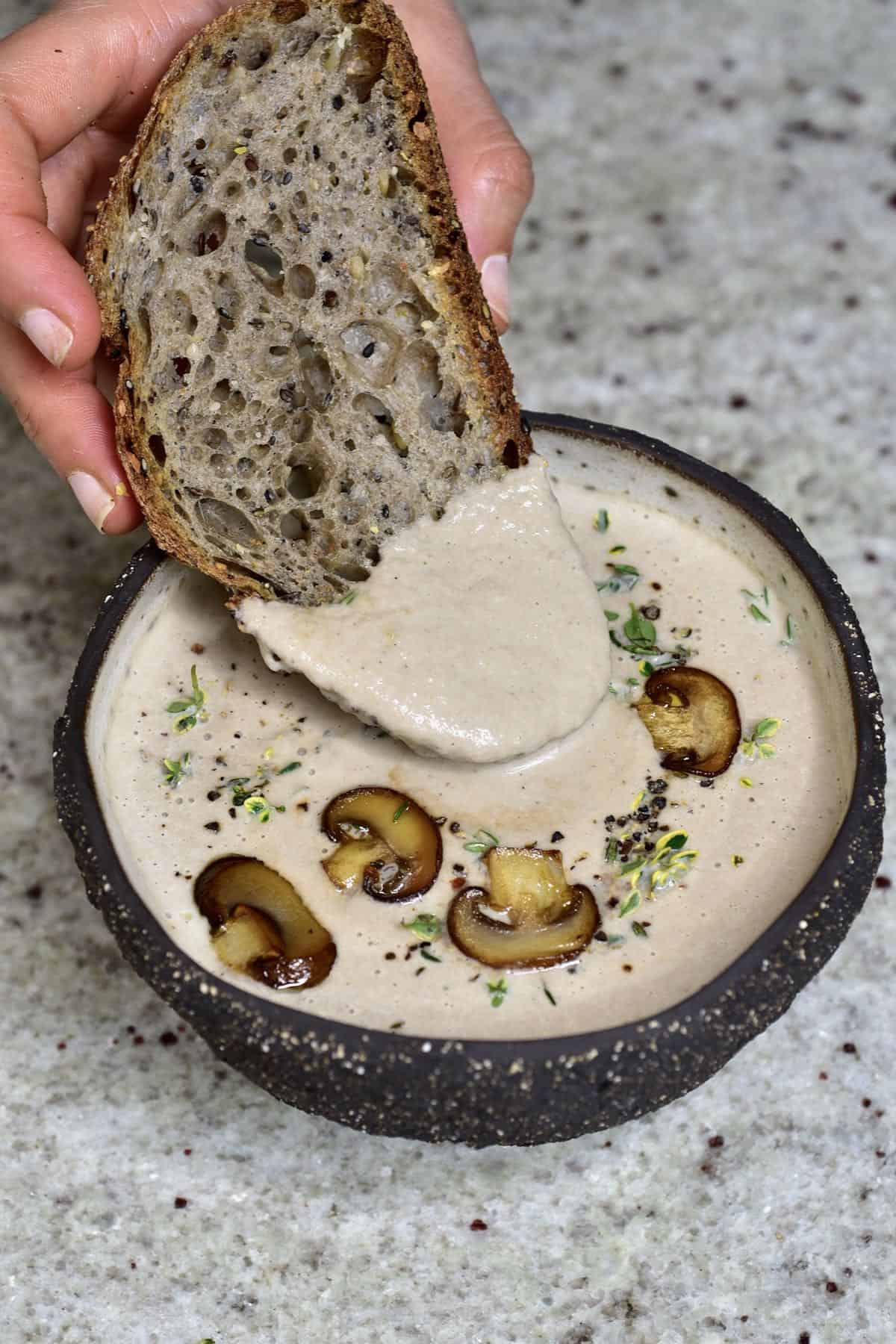 A bowl with mushroom soup and a piece of bread being dipped into it