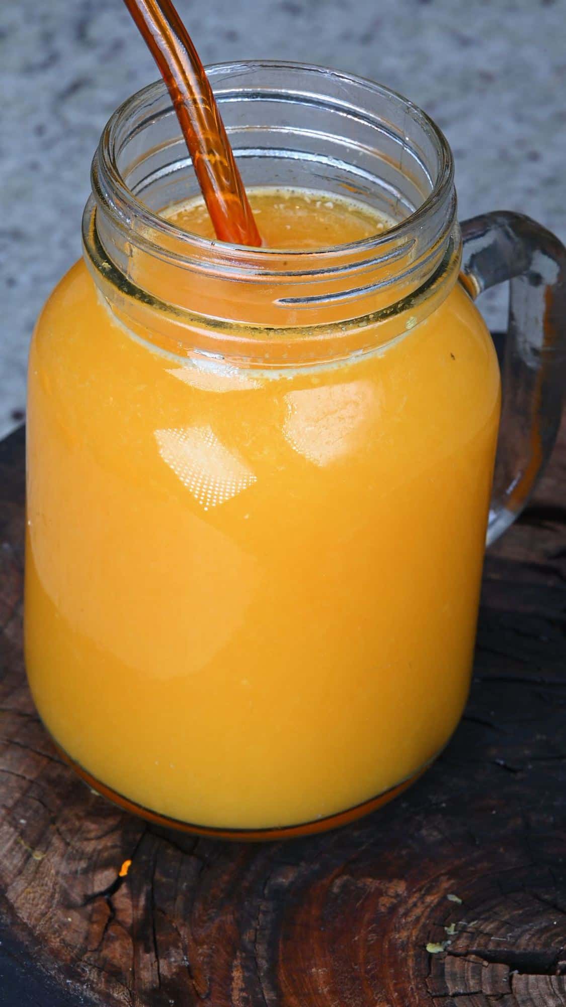 A mason jar with orange juice and a glass straw