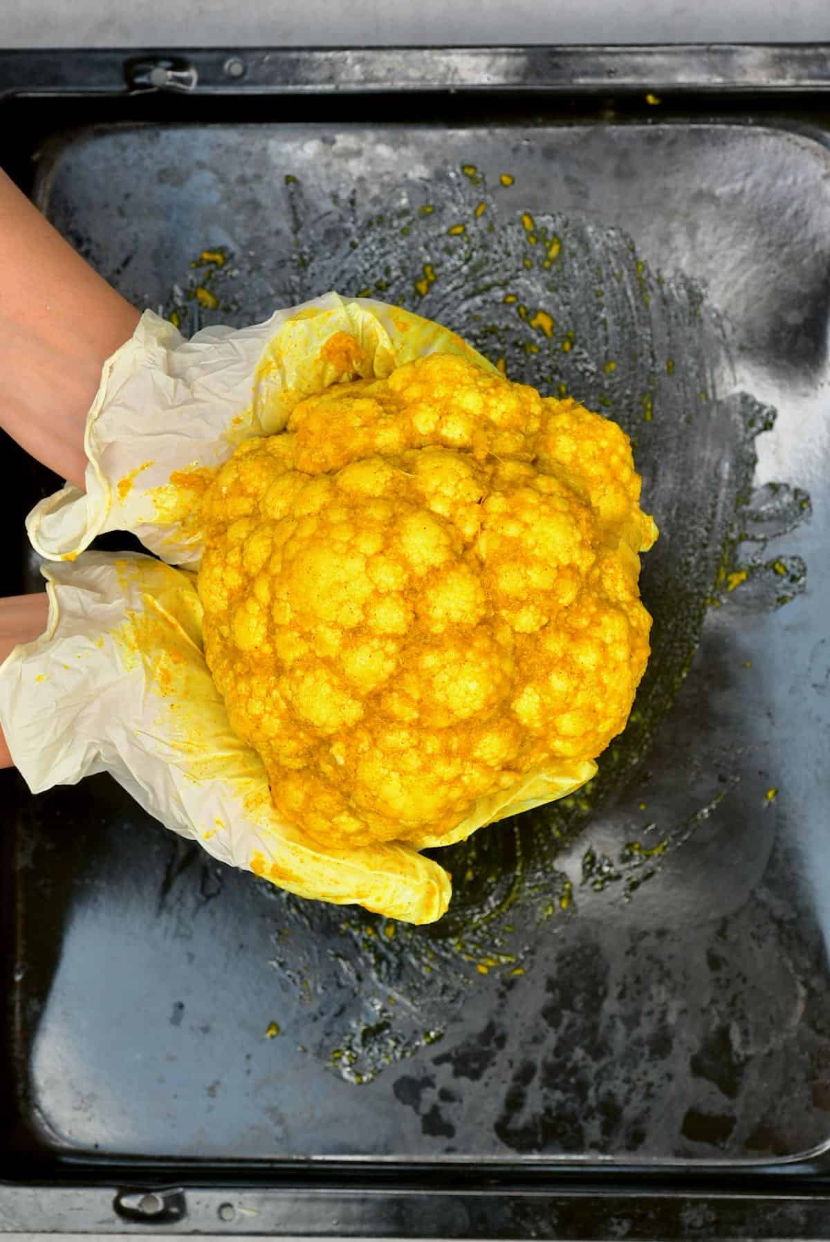 A cauliflower head covered with turmeric oil mixture over a baking tray