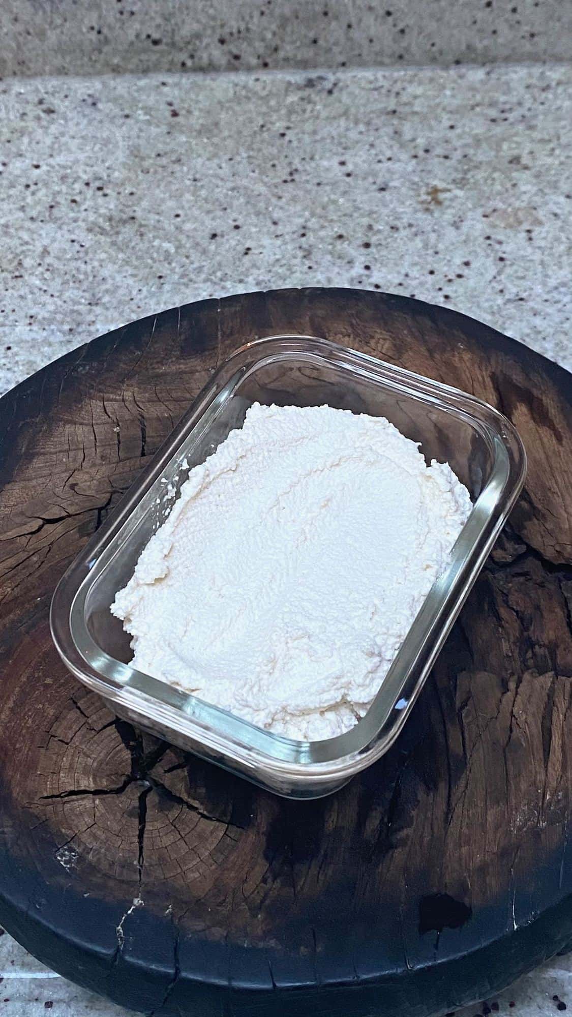 A glass container with vegan almond ricotta placed on a wooden board