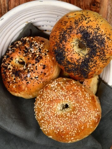 Three bagels over a grey towel in a white bowl