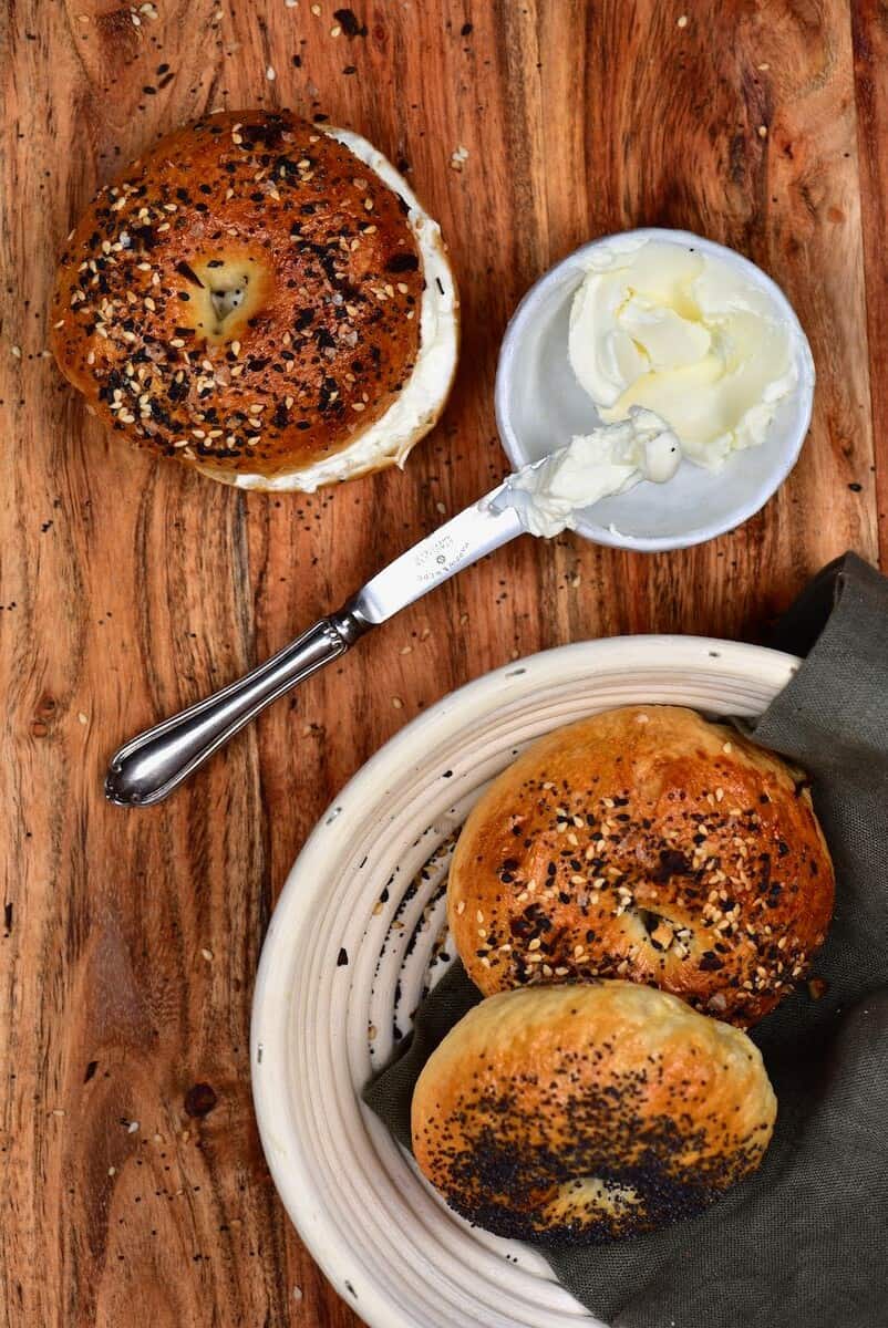 Bagel with cream cheese and a small bowl with cream cheese next to it