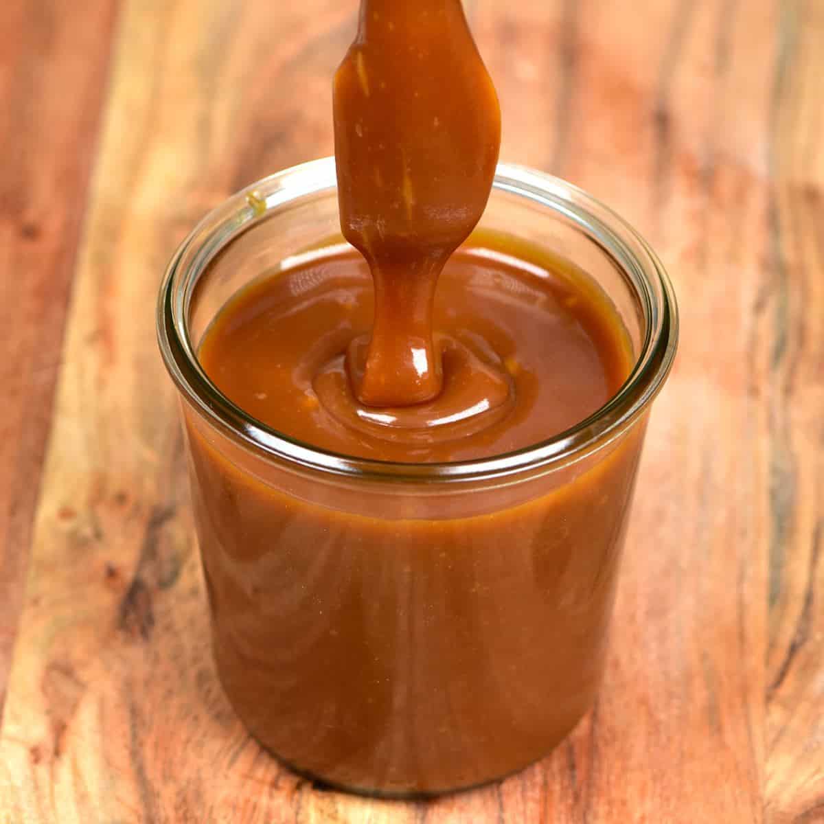 Dipping a spoon into a jar with homemade caramel