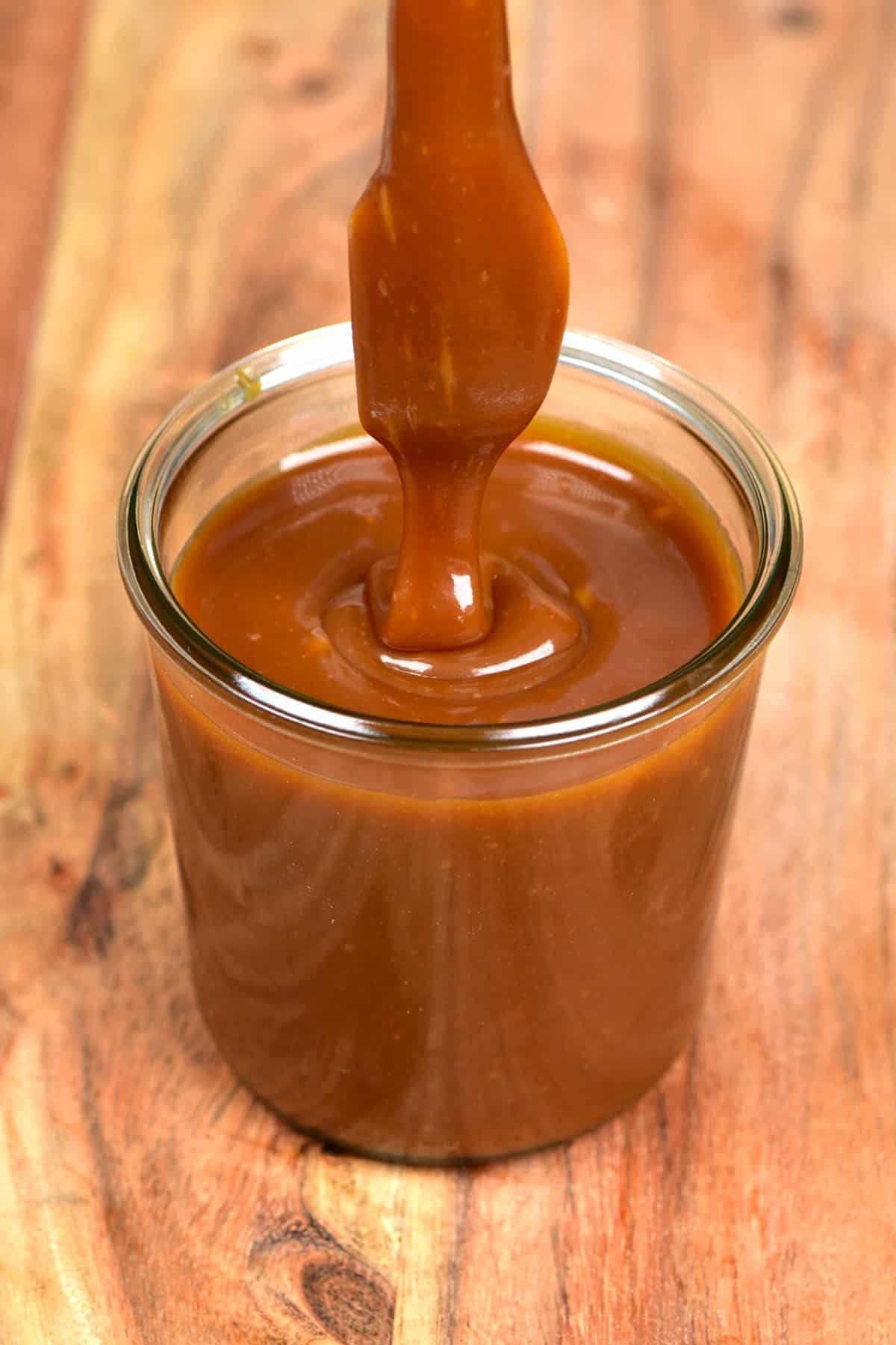 Dipping a spoon into a jar with homemade caramel