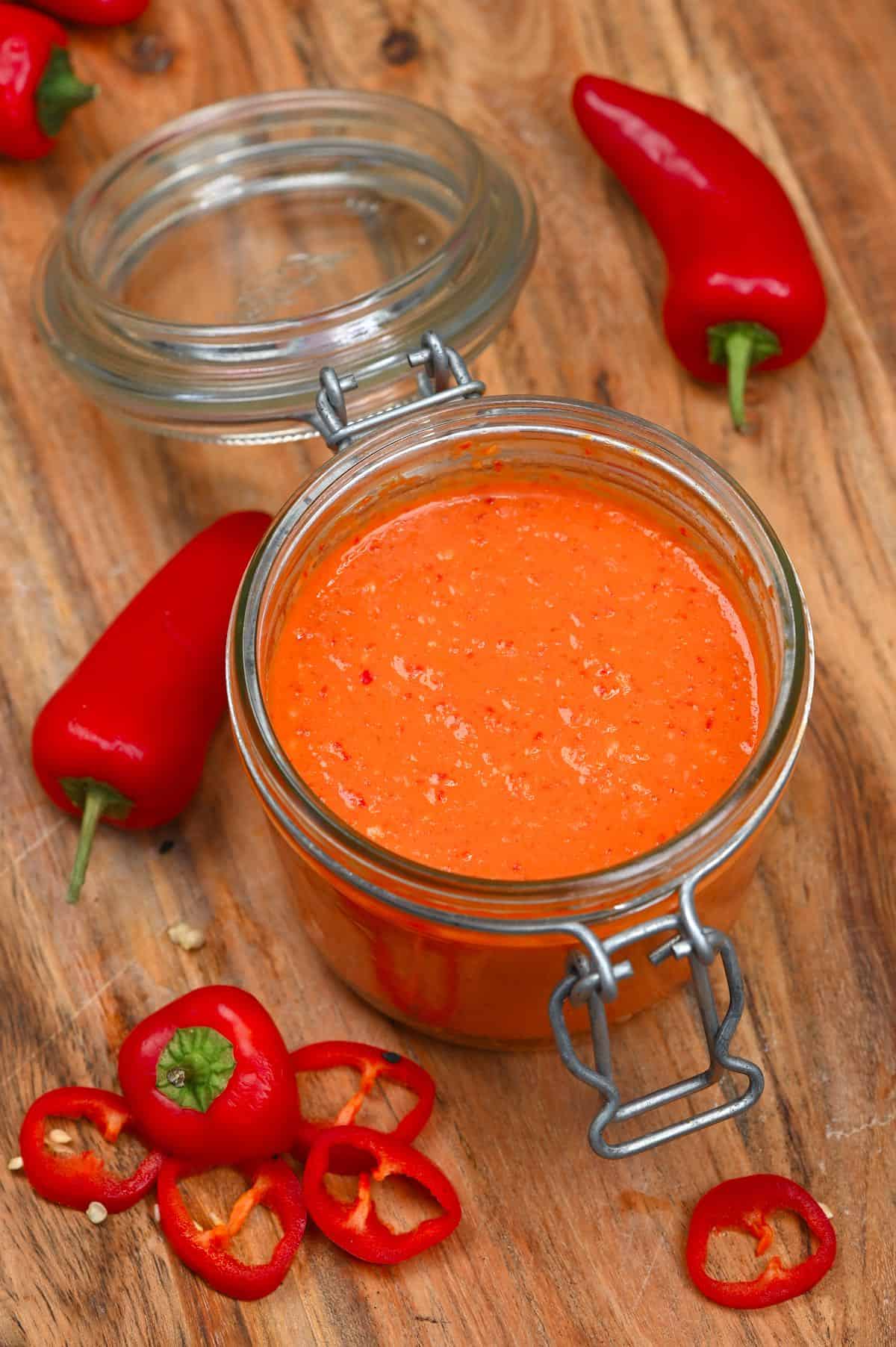 Homemade Red chilli sauce in a jar with some chilies around it