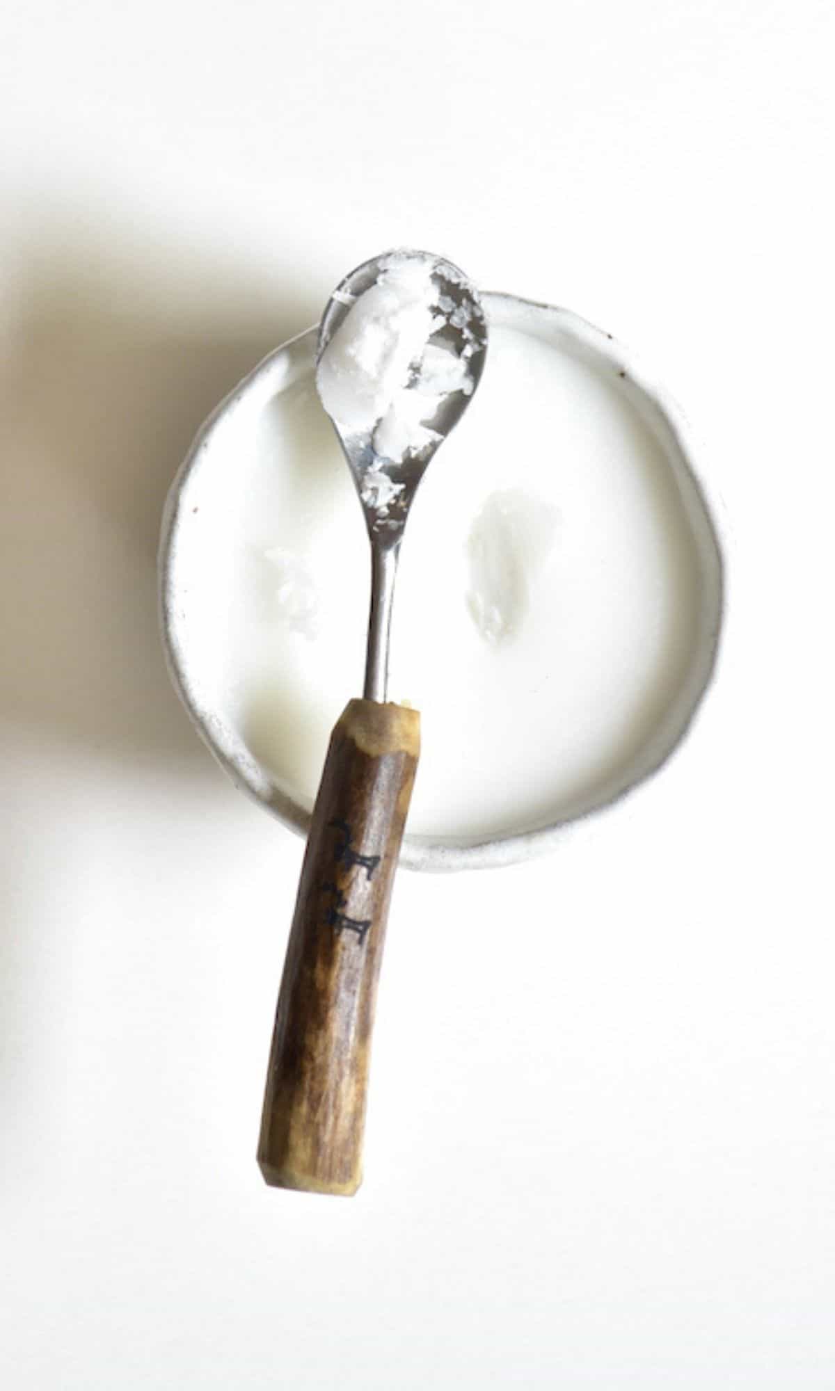 Extra virgin coconut oil in a spoon resting on a small bowl