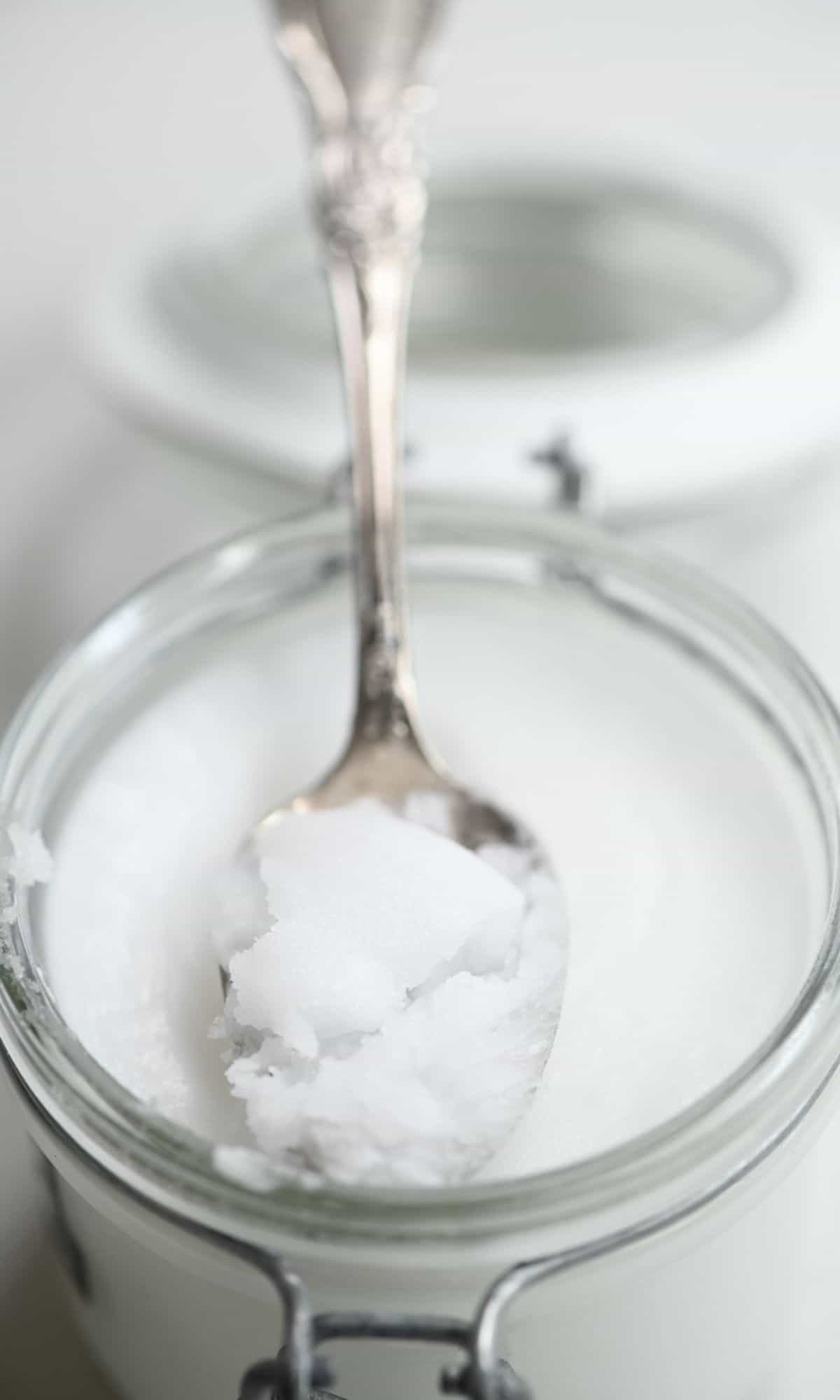 A spoonful of Extra virgin coconut oil resting on a jar