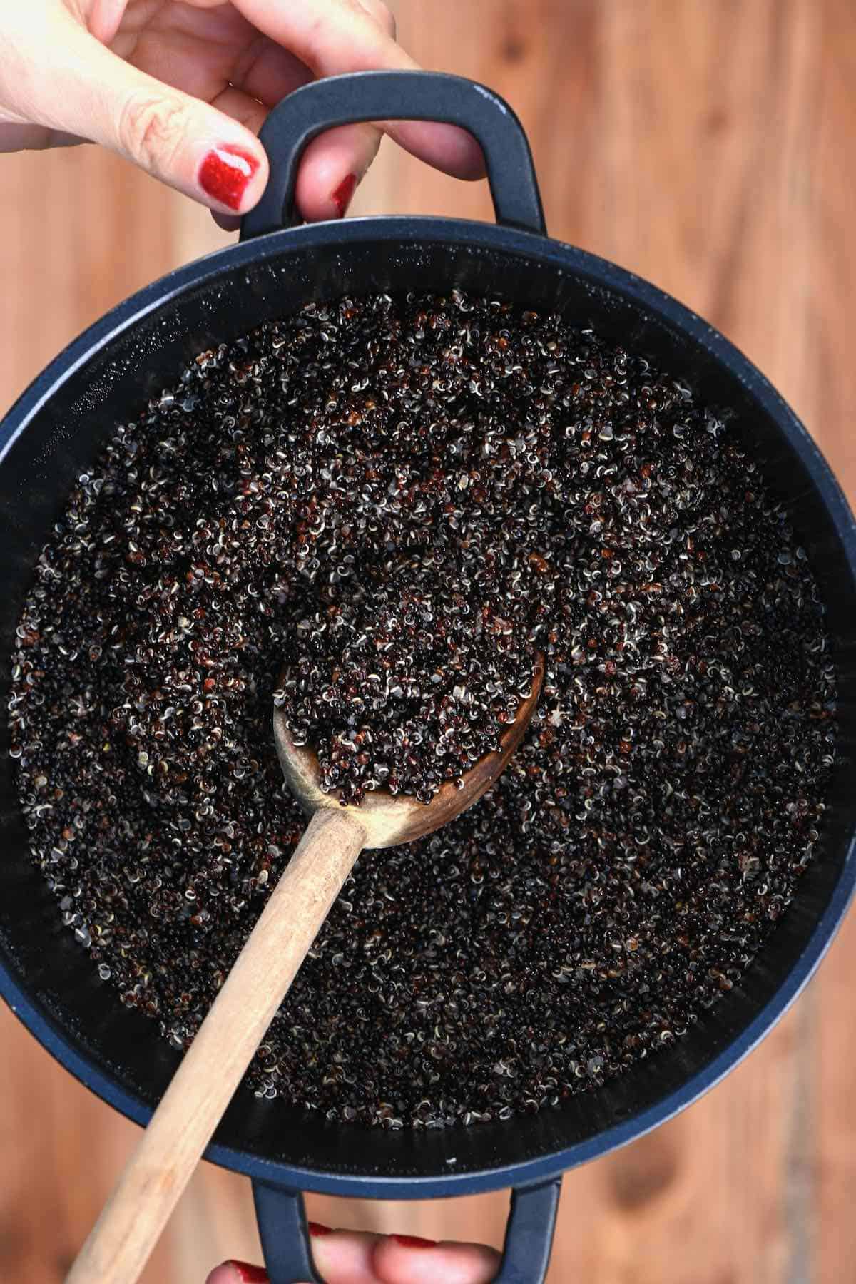 A pot with cooked quinoa and a wooden spoon