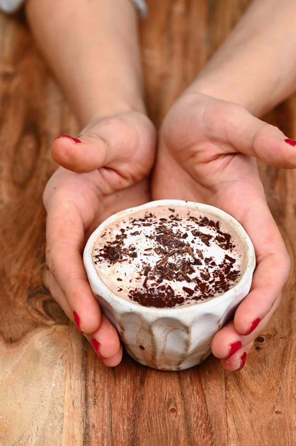 Hands holding a small cup with hot chocolate