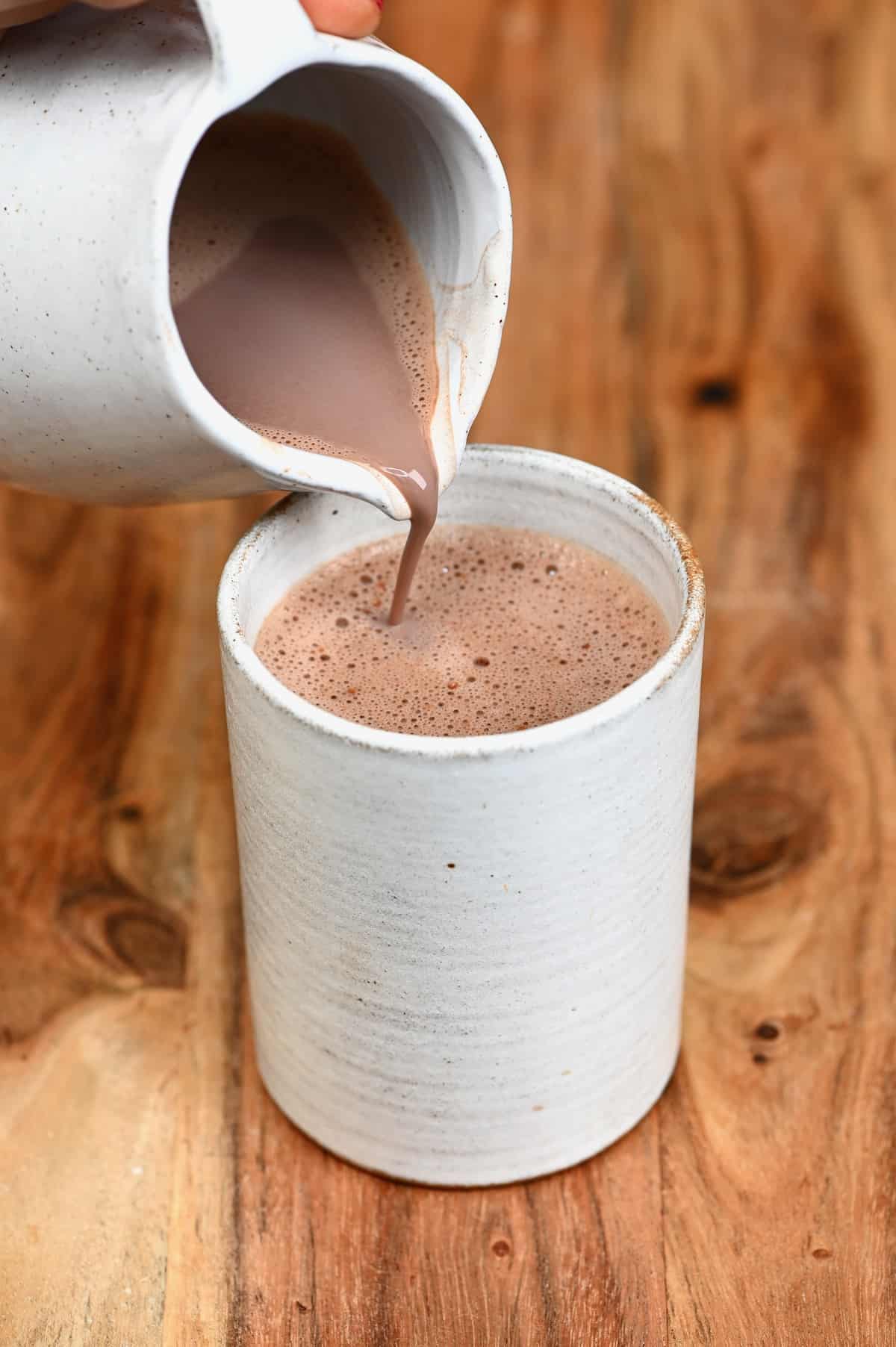 Pouring hot chocolate in a cup from a small pitcher