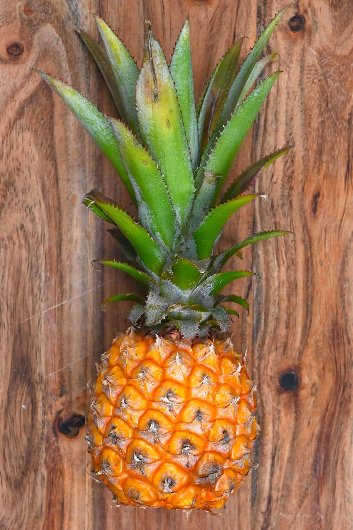 A small pineapple laying on a wooden board