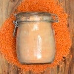 A jar with red lentil flour over some red lentils on a wooden board