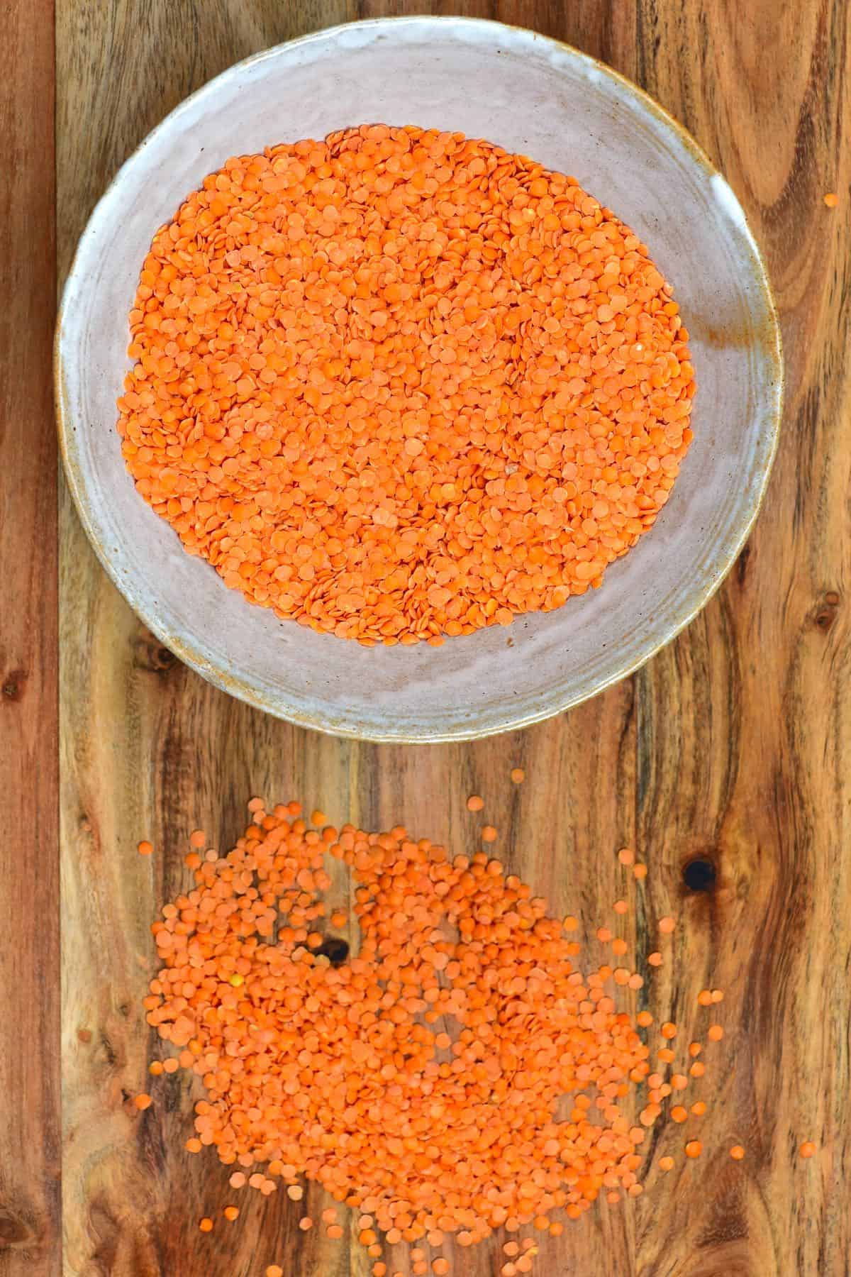 Red lentil beans in a bowl and sprinkled on a wooden board