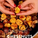 Peeling a roasted chestnut above a pan with other chestnuts
