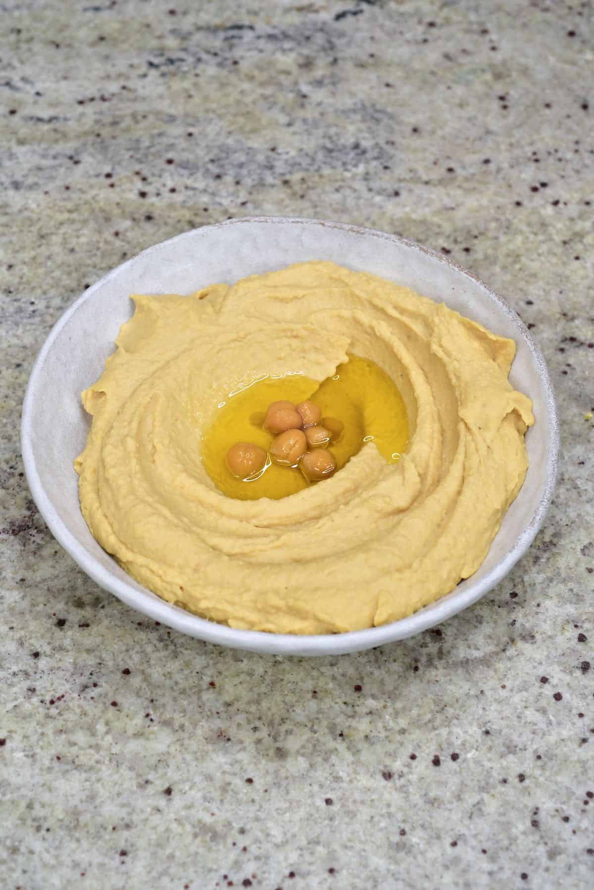 A bowl with hummus topped with some oil and chickpeas