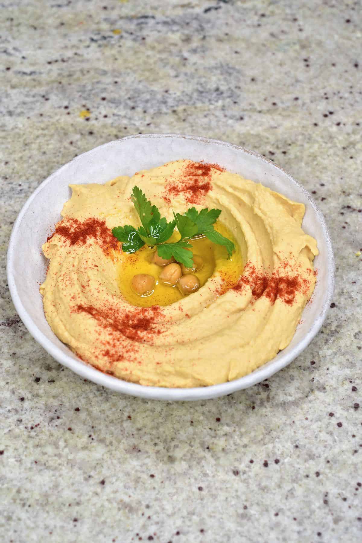 A bowl with hummus topped with some oil, chickpeas, paprika and coriander