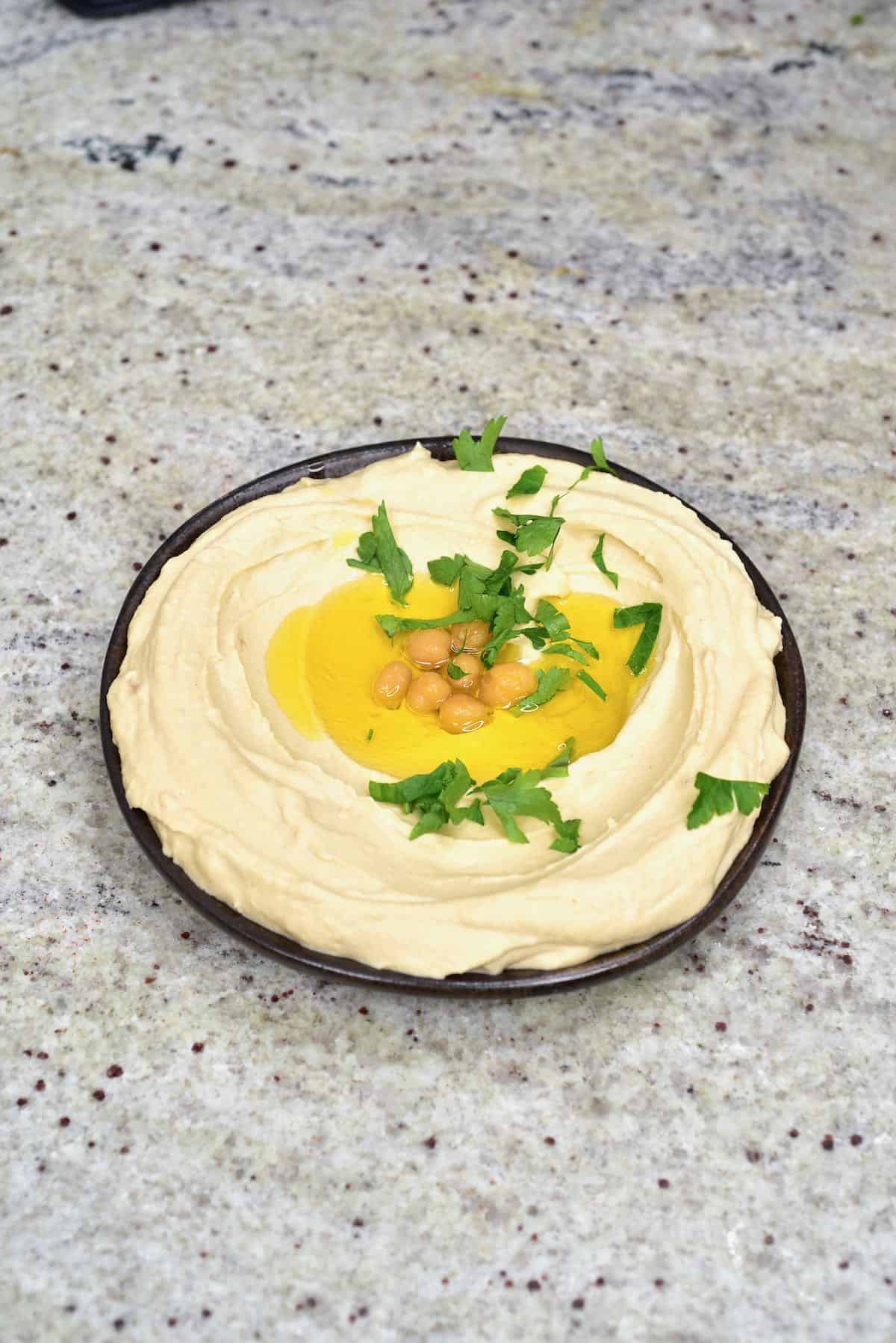 A bowl with hummus topped with some oil, chickpeas, and coriander