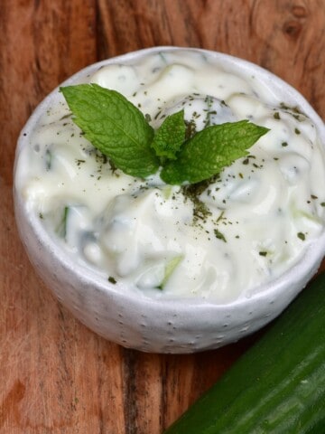 A small bowl with Yogurt Cucumber Salad topped with fresh mint leaves