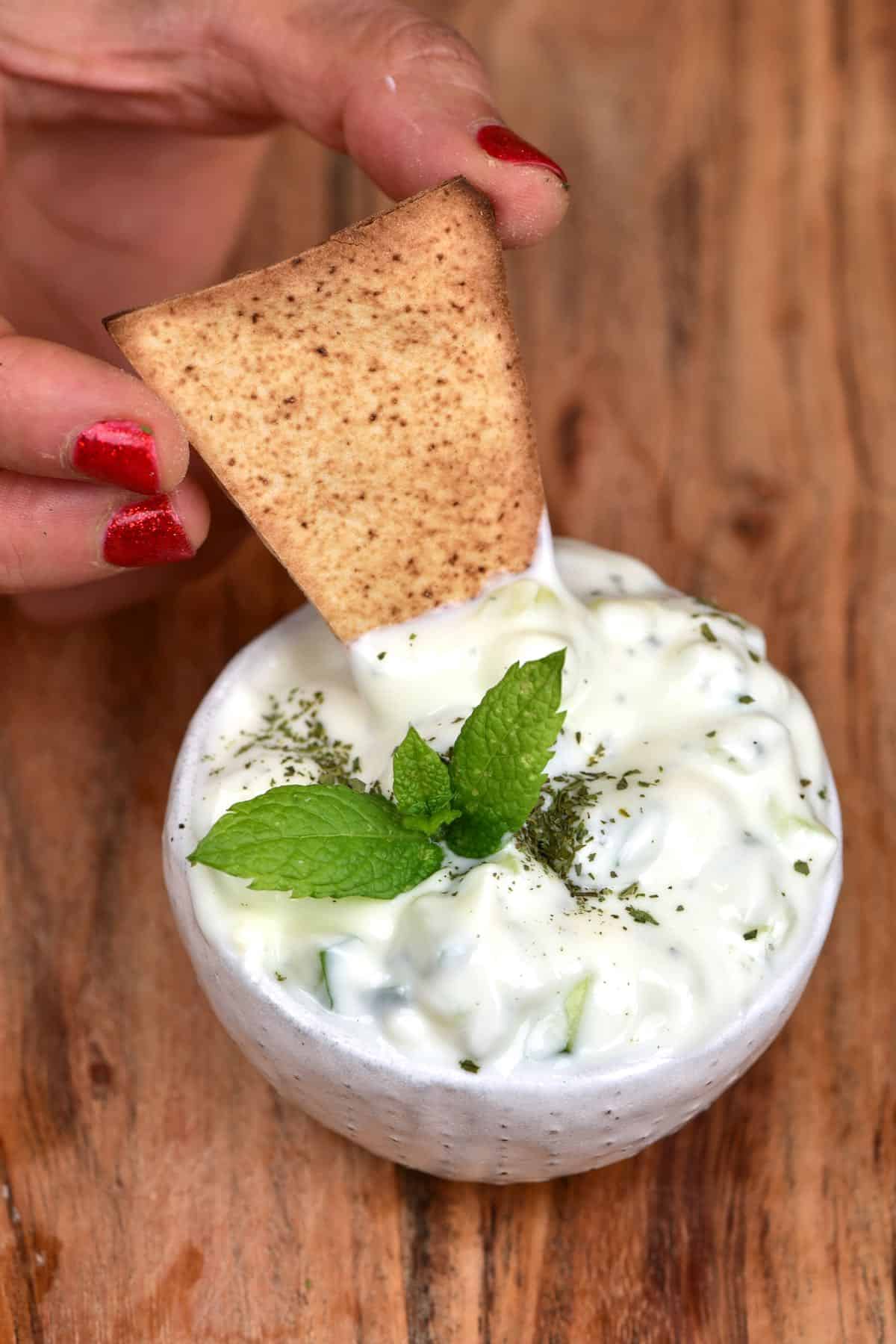 Dipping toasted pita bread into a small bowl with Yogurt Cucumber Salad
