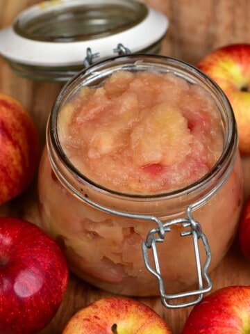 A jar with Applesauce and a few apples around it