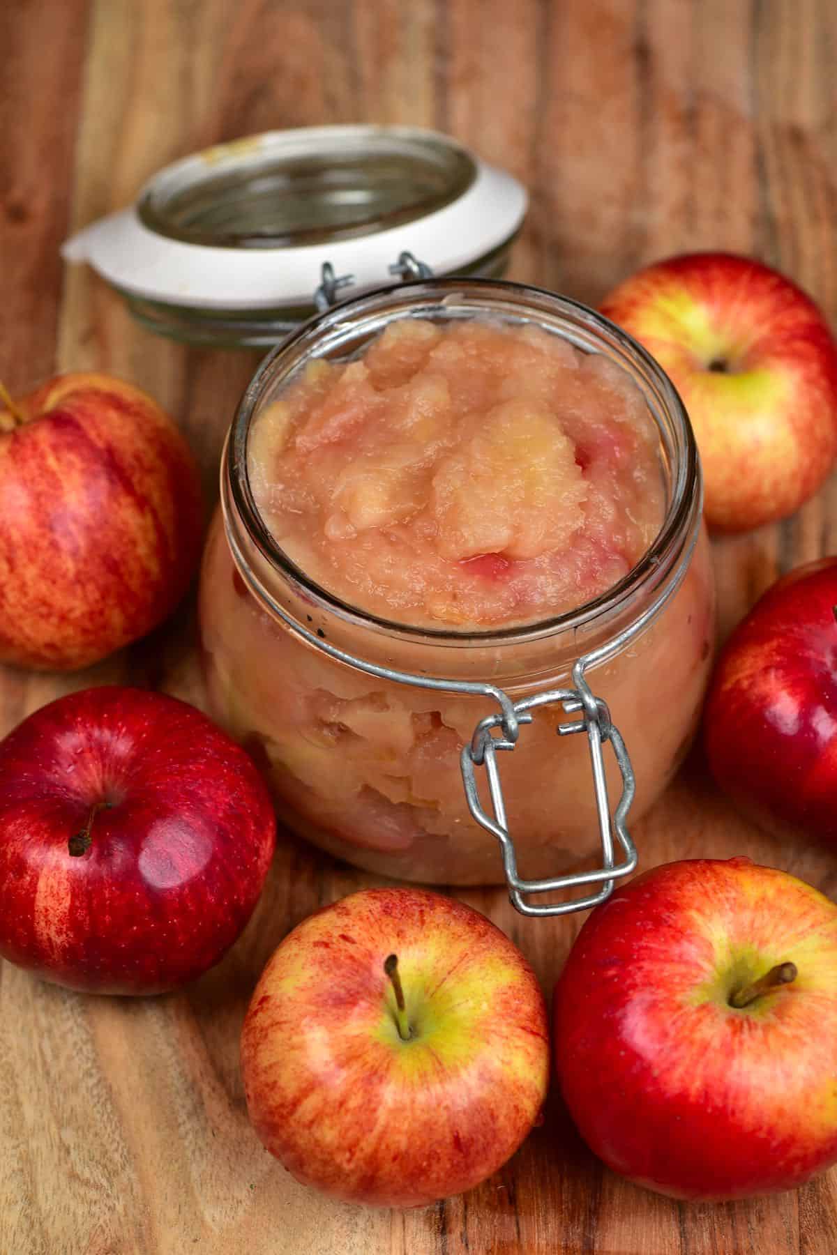 A jar with Applesauce and a few apples around it