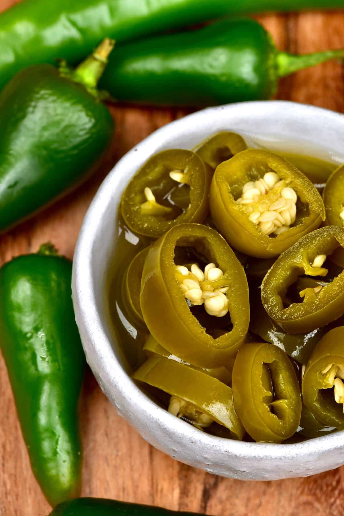 Pickled jalapeños in a bowl and some raw jalapeños next to them