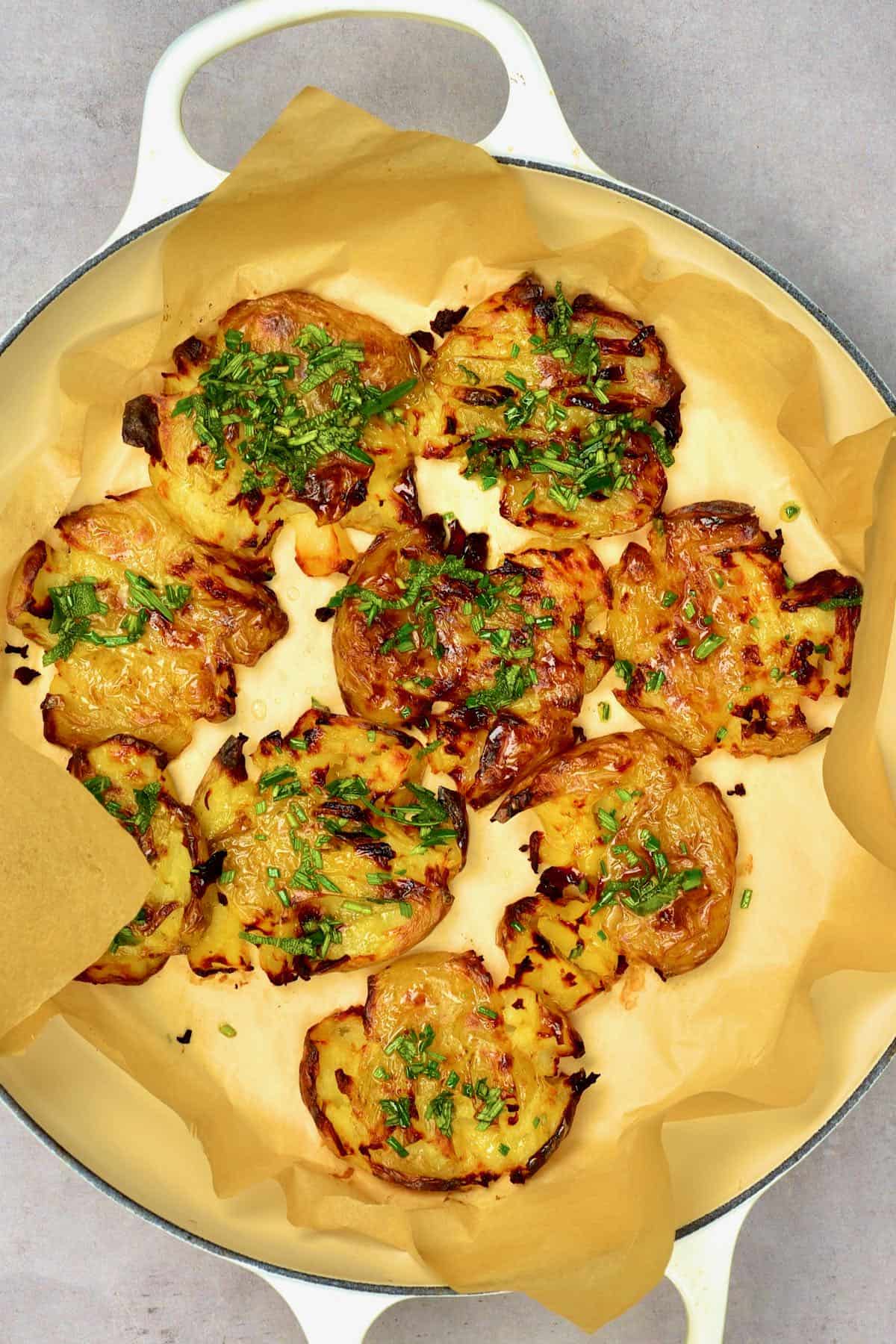 Baked smashed potatoes topped with thyme in an oven dish