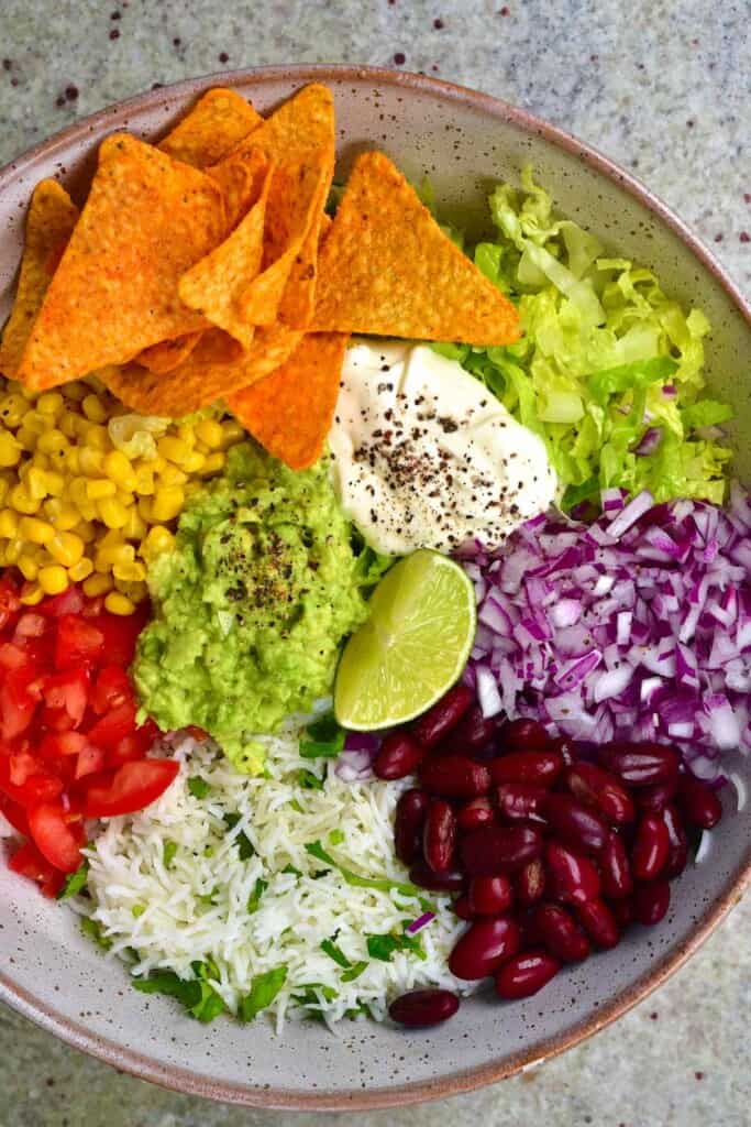 A bowl filled with rice, lettuce, corn, other veggies and corn chips