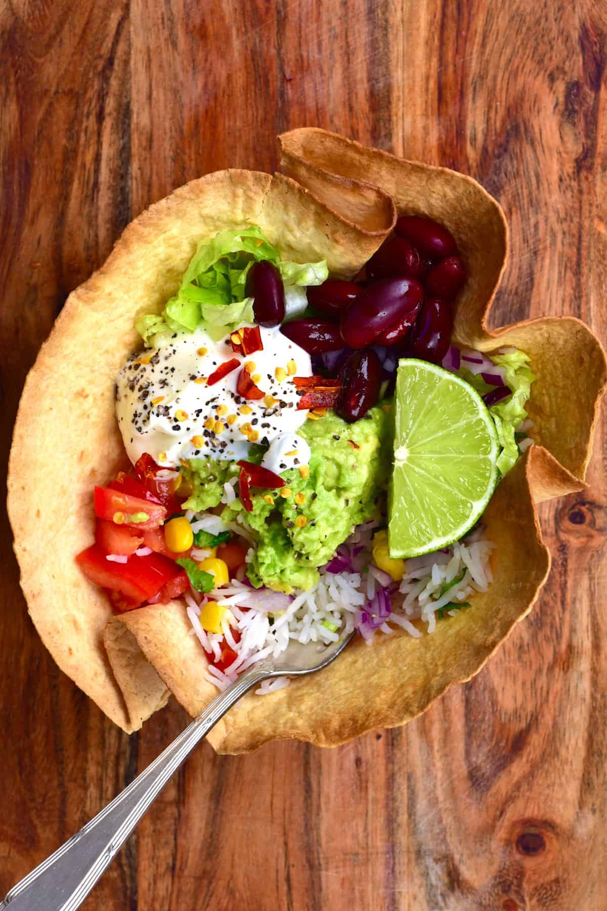 A toasted tortilla burrito bowl filled with rainbow veggies and a fork