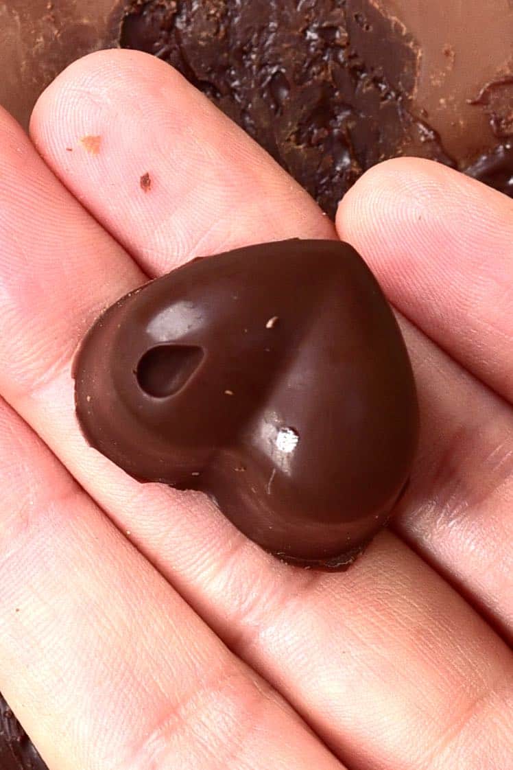 A hand holding a chocolate truffle heart
